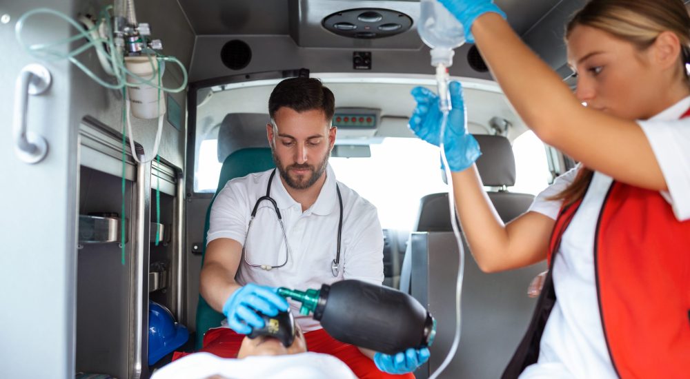 View from inside ambulance of uniformed emergency services workers caring for patient on stretcher during coronavirus pandemic.