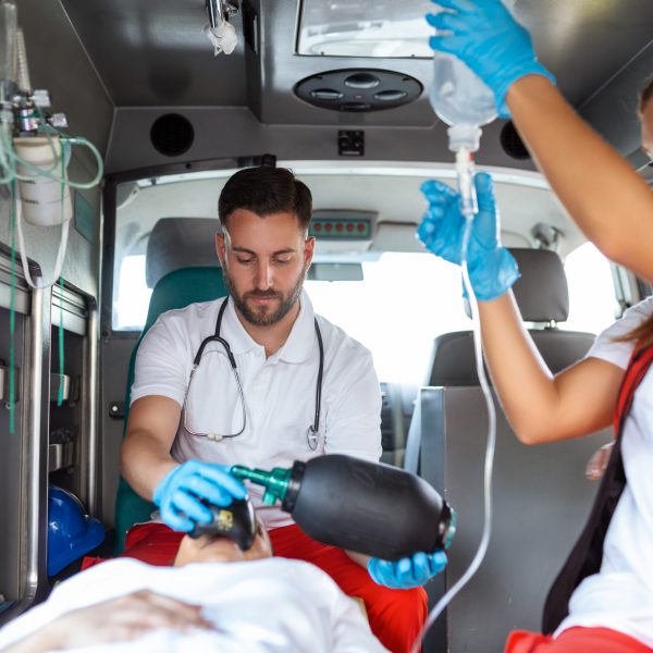 trasporto assistito di un paziente con ambulanza View from inside ambulance of uniformed emergency services workers caring for patient on stretcher during coronavirus pandemic.